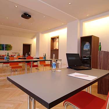 A bright modern meeting room with tables, orange chairs, and a laptop in the foreground.