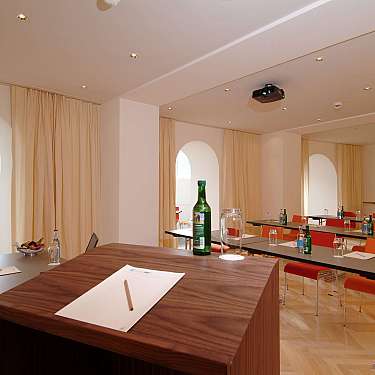 Bright seminar room with tables, red chairs, projector, and notebooks set out