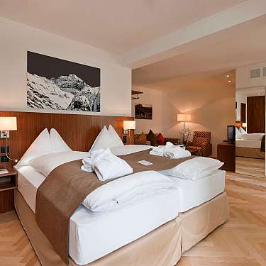 Helles Hotelzimmer mit Doppelbett, braunen Bettdecken und angrenzender Sauna mit Glastür