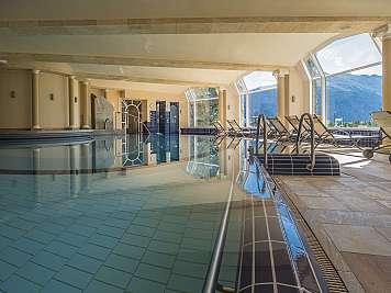 Luxuriöser Innenpool mit Liegen und großen Fenstern zum Bergpanorama.