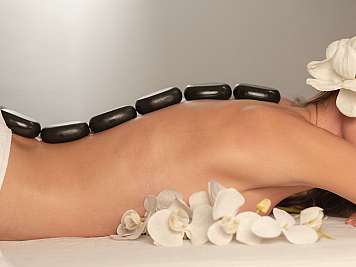 Rückenmassage mit heißen Steinen und weißen Blüten auf einer Liege