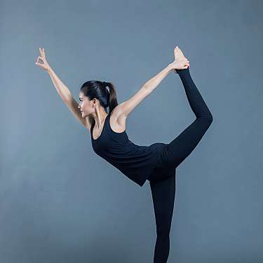 Frau in schwarzer Sportkleidung hält eine Yoga-Balancepose auf einer pinken Matte.