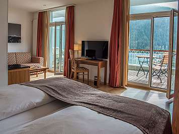 Gemütliches Hotelzimmer mit Bett, Fernseher, Schreibtisch und Balkon mit Bergblick.