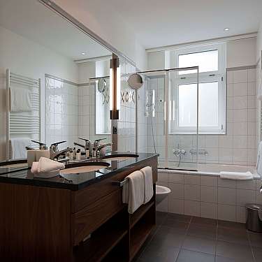 Bright modern bathroom with double sink, mirror, bathtub, and white towels.