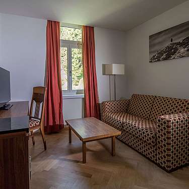Kleines Wohnzimmer mit Sofa, Couchtisch, Fernseher, Fenster und Stehlampe.