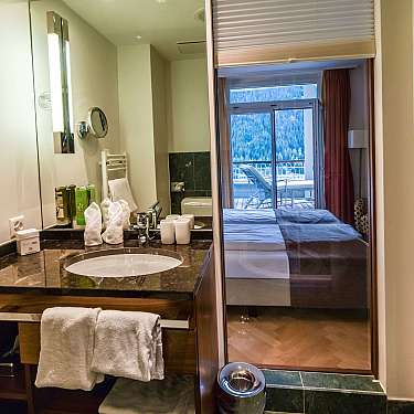 Modern hotel bathroom with sink, towels, and a view into the bedroom and balcony