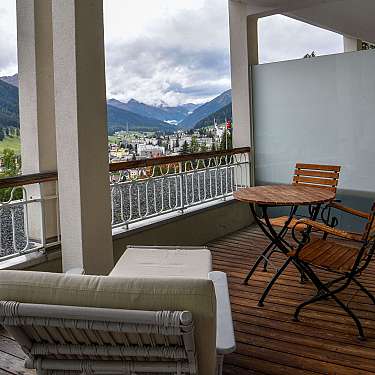 Wooden balcony seating overlooks a mountain town and cloudy valley.