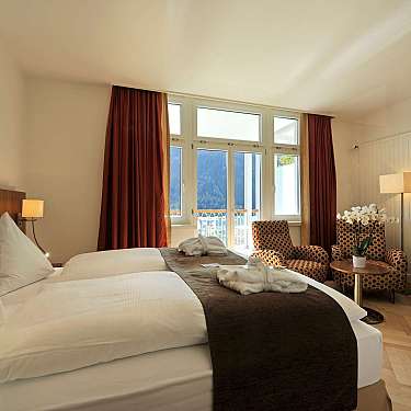 Neat hotel room with twin beds, wooden desks, and an open balcony door to a mountain view.