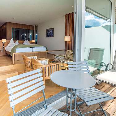 Bright hotel room with bed, seating area, and balcony furniture