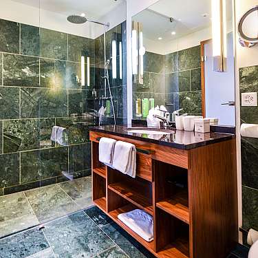 Modern bathroom with glass shower, wooden vanity, and green stone tiles.