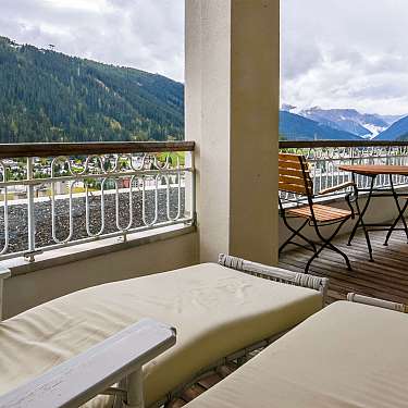 Balcony with lounge chairs and table overlooking forested mountains and a valley