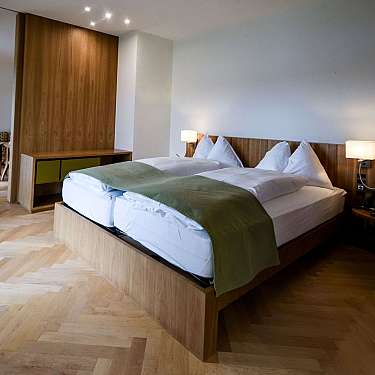 Neatly made double bed in a modern hotel room with wooden furniture and lamps.